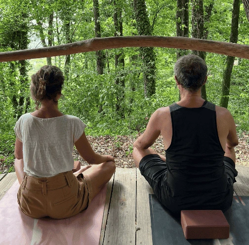 Deux personnes assises en tailleur sur un tapis de yoga face à la nature