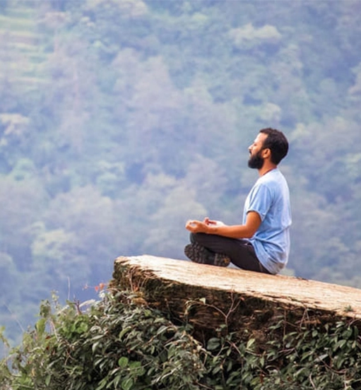 Personne en méditation assise sur un rocher face à la nature