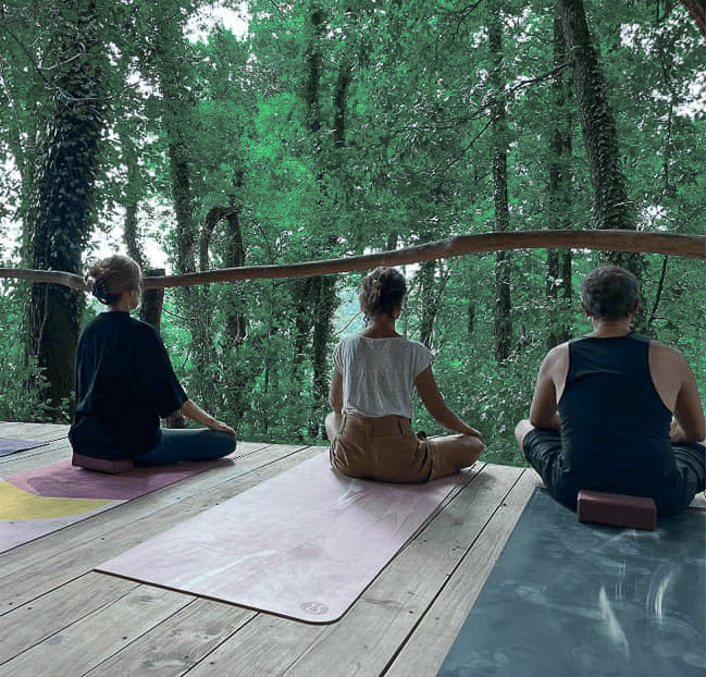 Trois personnes assises en tailleur sur un tapis de yoga face à la nature